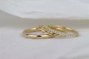 Zu sehen sind drei Ringe in Gelbgold: ein schlichter, abgerundeter Ehering mit glänzender Oberfläche, ein Beisteckring mit zwei ineinander verflochtenen Drähten und ein feiner Memoryring mit vielen kleinen Brillanten.