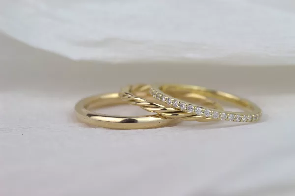 Zu sehen sind drei Ringe in Gelbgold: ein schlichter, abgerundeter Ehering mit glänzender Oberfläche, ein Beisteckring mit zwei ineinander verflochtenen Drähten und ein feiner Memoryring mit vielen kleinen Brillanten.