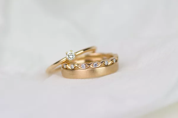 Zu sehen sind drei Ringe, die man schön zusammentragen kann. Alle aus Roségold. Ein schlichter Ehering mit matter Oberfläche, ein besonderer Beisteckring mit vielen Diamanten und ein Verlobungsring mit einem großen Brillanten.