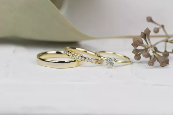 Elegante Verbindung: 585er Gelbgold-Eheringe, poliert, Damenring mit funkelnden Brillanten im Memory-Stil. Im Bild erkennt man außerdem einen Ring mit einem großen Diamanten, ein Verlobungsring.