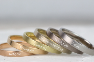 Das Bild zeigt Eheringe in verschiedenen Edelmetallfarben - Gold, Gelbgold, Roségold, Rotgold, Champagnergold, Weißgold und Platin.