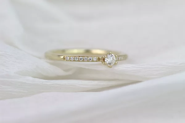 Eleganter Verlobungsring aus Gelbgold mit einem funkelnden Diamanten in der Mitte und zahlreichen kleinen Brillanten, die die Ringschiene zieren.