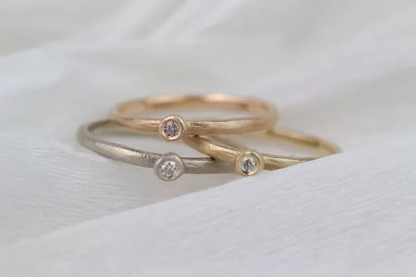 Drei Verlobungsringe mit natürlicher, matter Oberfläche und Zargenfassung. In Rotgold, Weißgold und Gelbgold mit verschieden farbigen Diamanten.