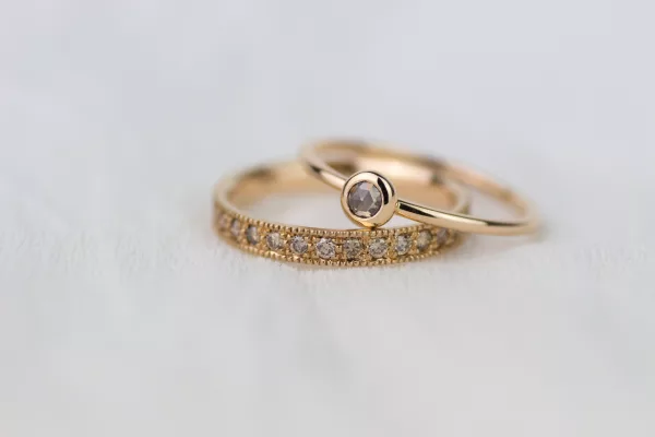 Zu erkennen sind zwei Ringe in Roségold und Rotgold. ein Ehering im Vintage-Stil, ausgefasst mit champagnerfarbenen Diamanten. Und ein Verlobungsring mit einer Zargenfassung und einem braunen Diamant im Rosenschliff.