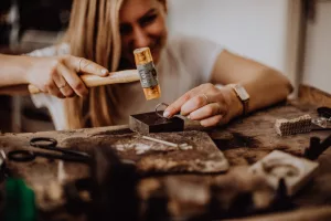 Man sieht eine Goldschmiedin beim Arbeiten: Sie schmiedet einen Ring mit einem Hammer.